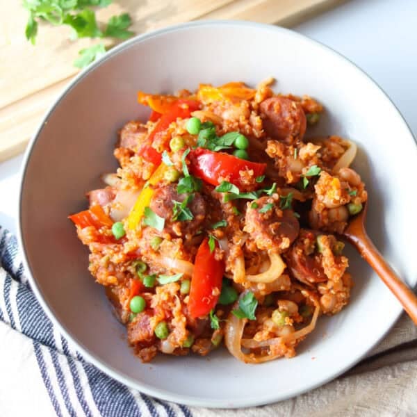 A serving of finished slow cooker sausage casserole in a white serving bowl with a wooden spoon sitting in it.