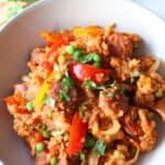 A serving of finished slow cooker sausage casserole in a white serving bowl with a wooden spoon sitting in it.