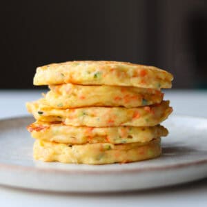 A stack of 5 cooked savory cheese pancakes sitting on a cream plate.