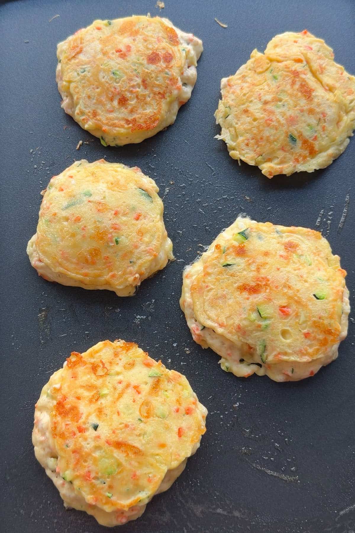 Five pancakes on a skillet that have been flipped over.