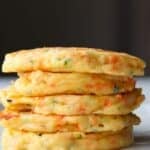 A stack of 5 cooked savory cheese pancakes sitting on a cream plate.