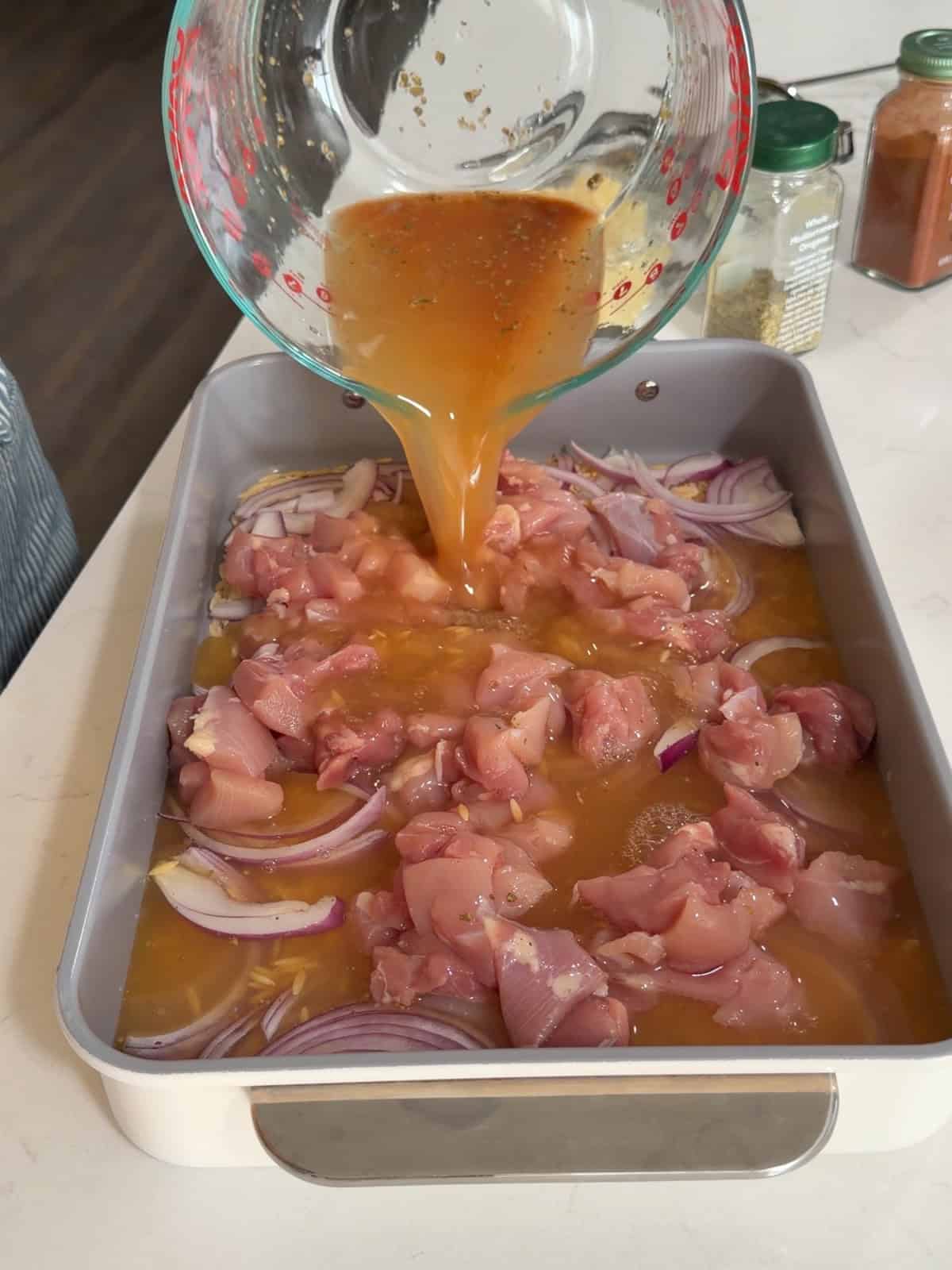 Chicken broth being poured on top of chicken orzo and onion.