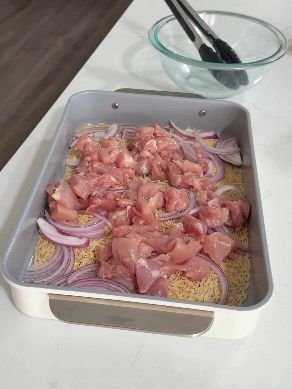 Orzo, chicken, and onion in large baking pan.