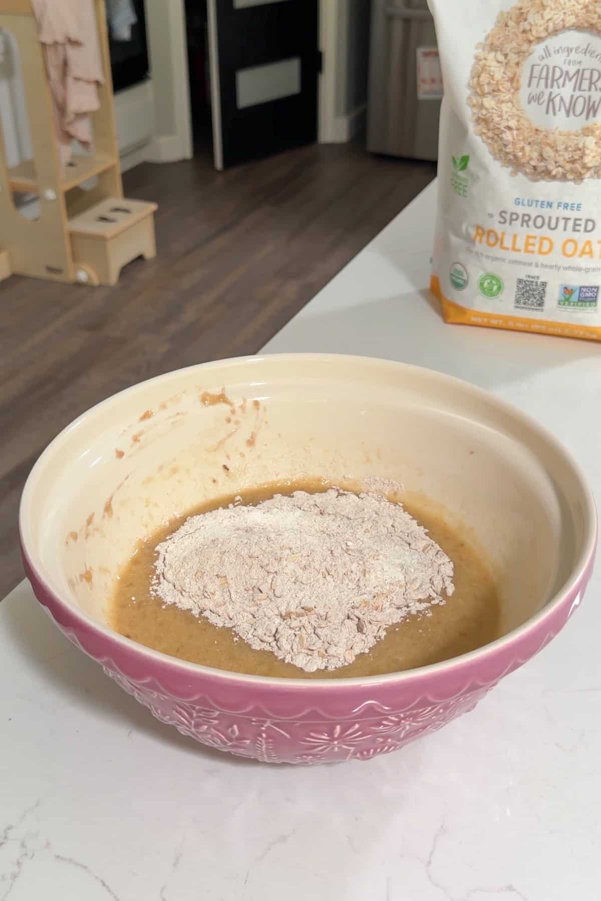 Dry ingredients added to wet ingredients in a large purple bowl.