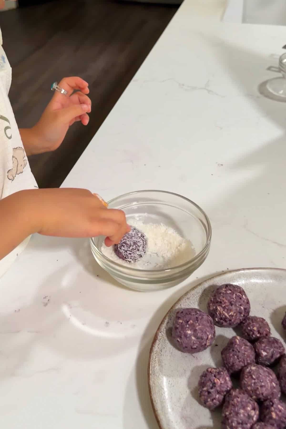 A child rolling the ball in shredded coconut.