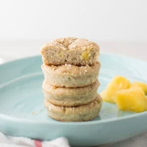 Four pineapple coconut muffins stacked on a blue plate with a bite taken out of the top muffin.