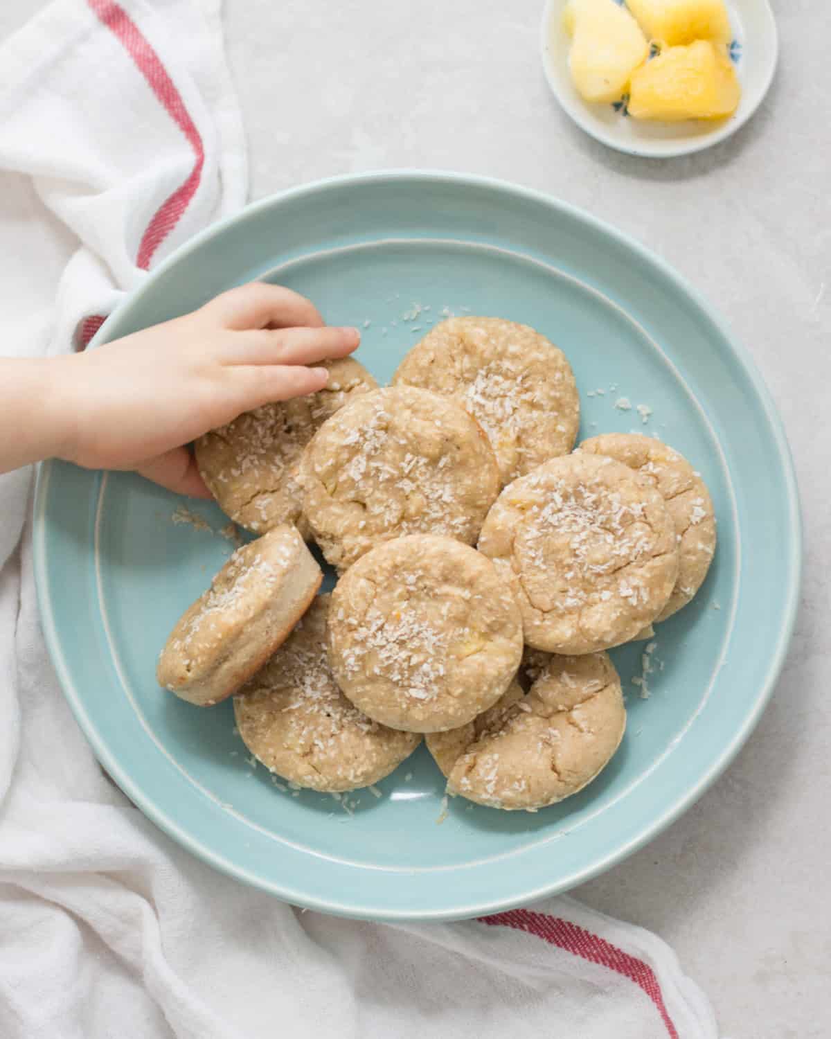 Pineapple coconut muffins placed on a blue plate with a toddler's hand grabbing one.
