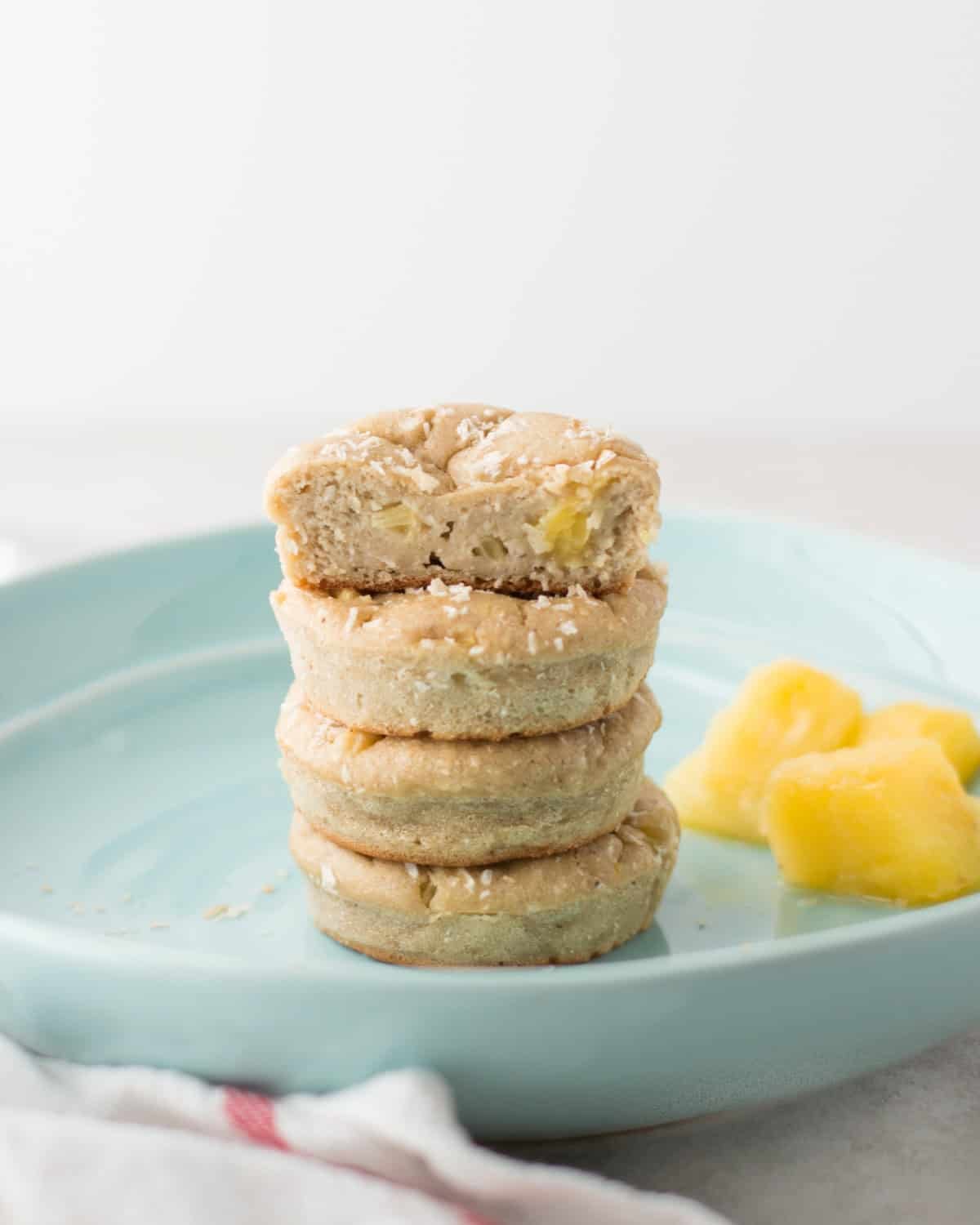 Four pineapple coconut muffins stacked on a blue plate with a bite taken out of the top muffin.