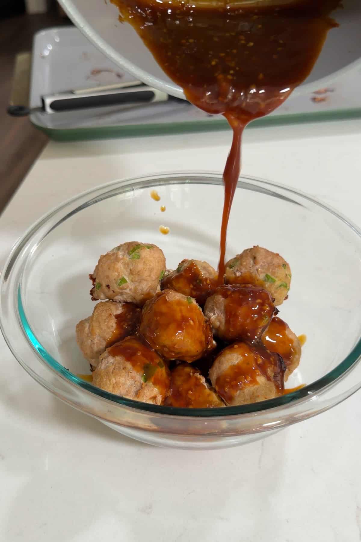Teriyaki sauce poured over the cooked meatballs in a glass bowl.