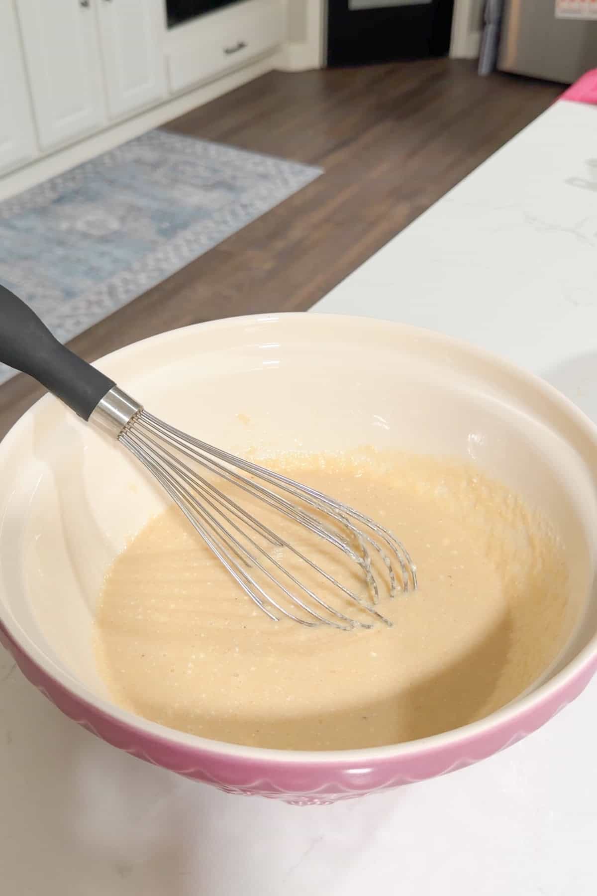 A large mixing bowl holding applesauce, Greek yogurt, eggs, melted butter, maple syrup, and vanilla, being whisked into a smooth batter.
