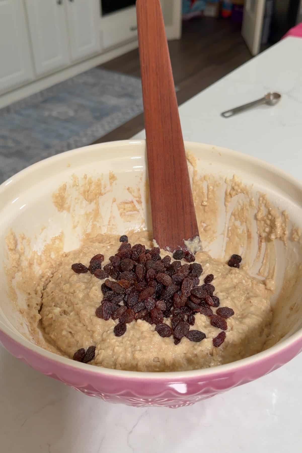 The batter for the muffins in a large mixing bowl with raisins added to it.