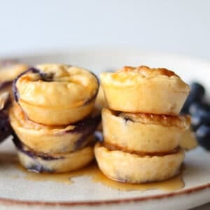 Stacked cottage cheese bites on a white plate with drizzle of maple syrup.
