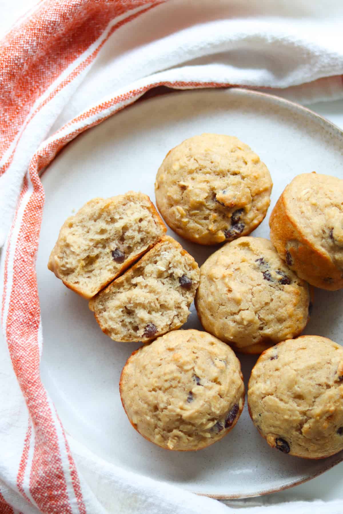 Applesauce muffins on a white plate, with one torn in half to reveal the inside.