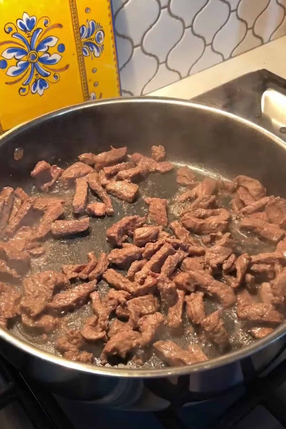 Sliced beef cooking in a large deep pan.