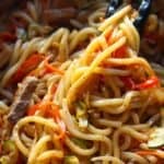 Cooked beef udon stir fry picked up with a tong.