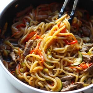 Cooked beef udon stir fry picked up with a tong.