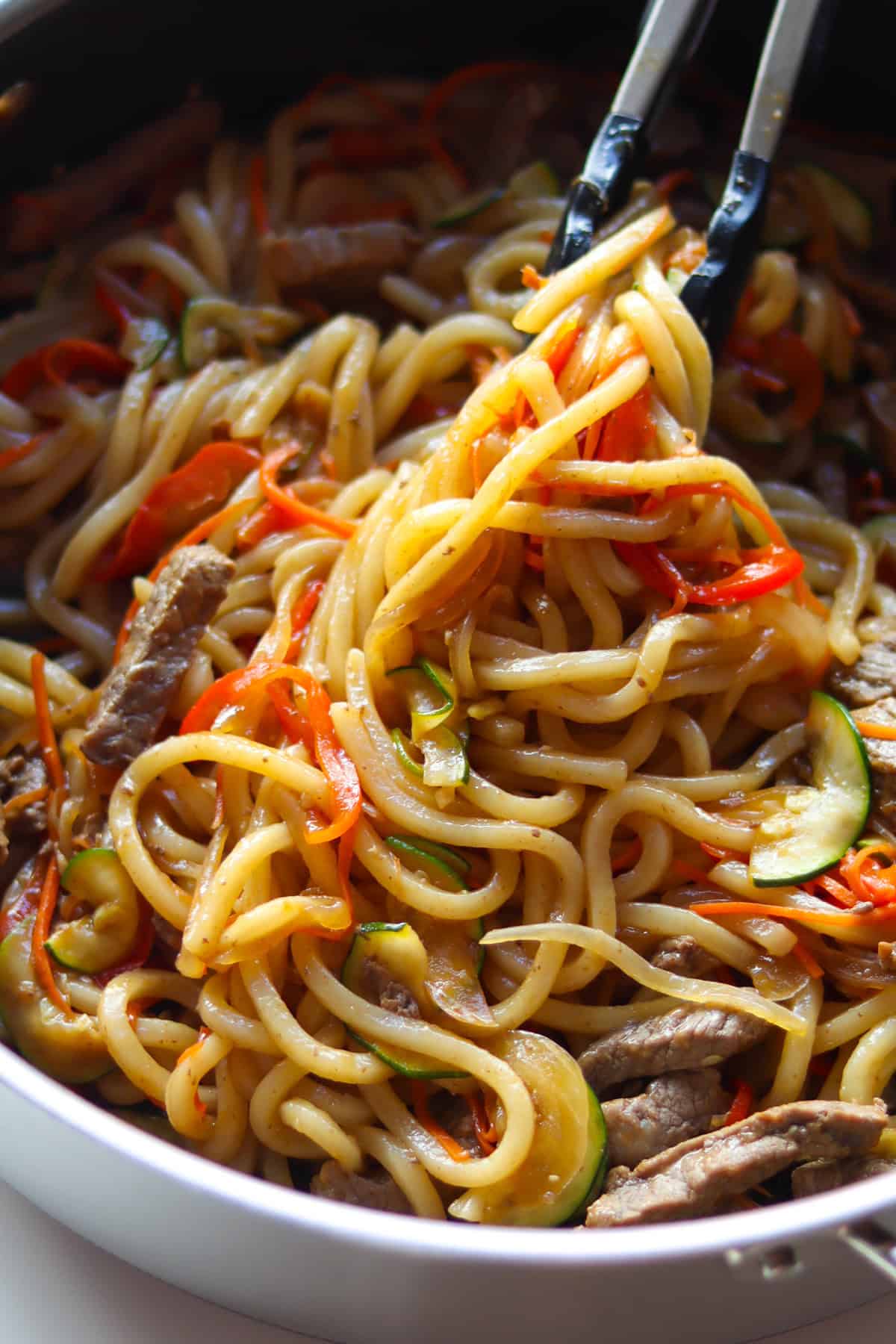 Cooked beef udon stir fry picked up with a tong.