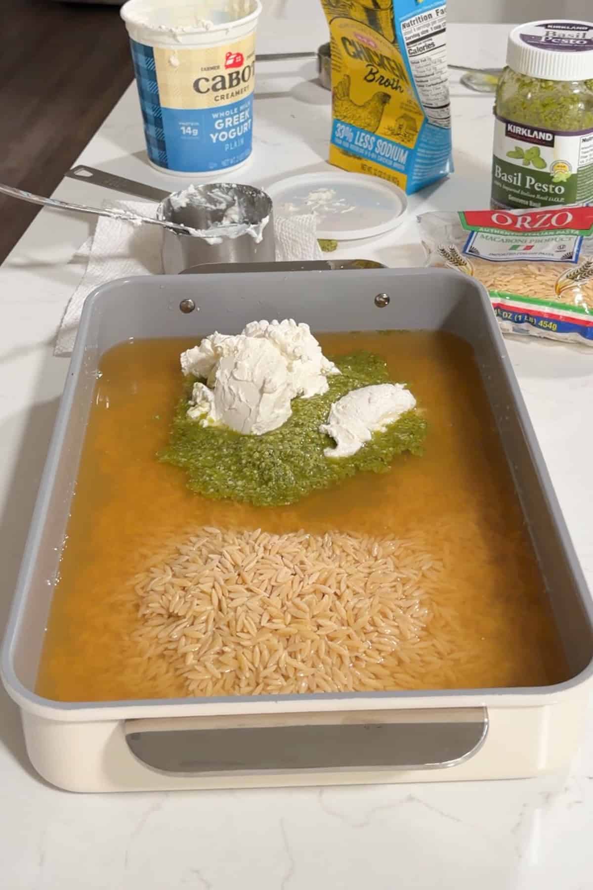 Orzo in broth with pesto and Greek yogurt on top in a large baking pan.