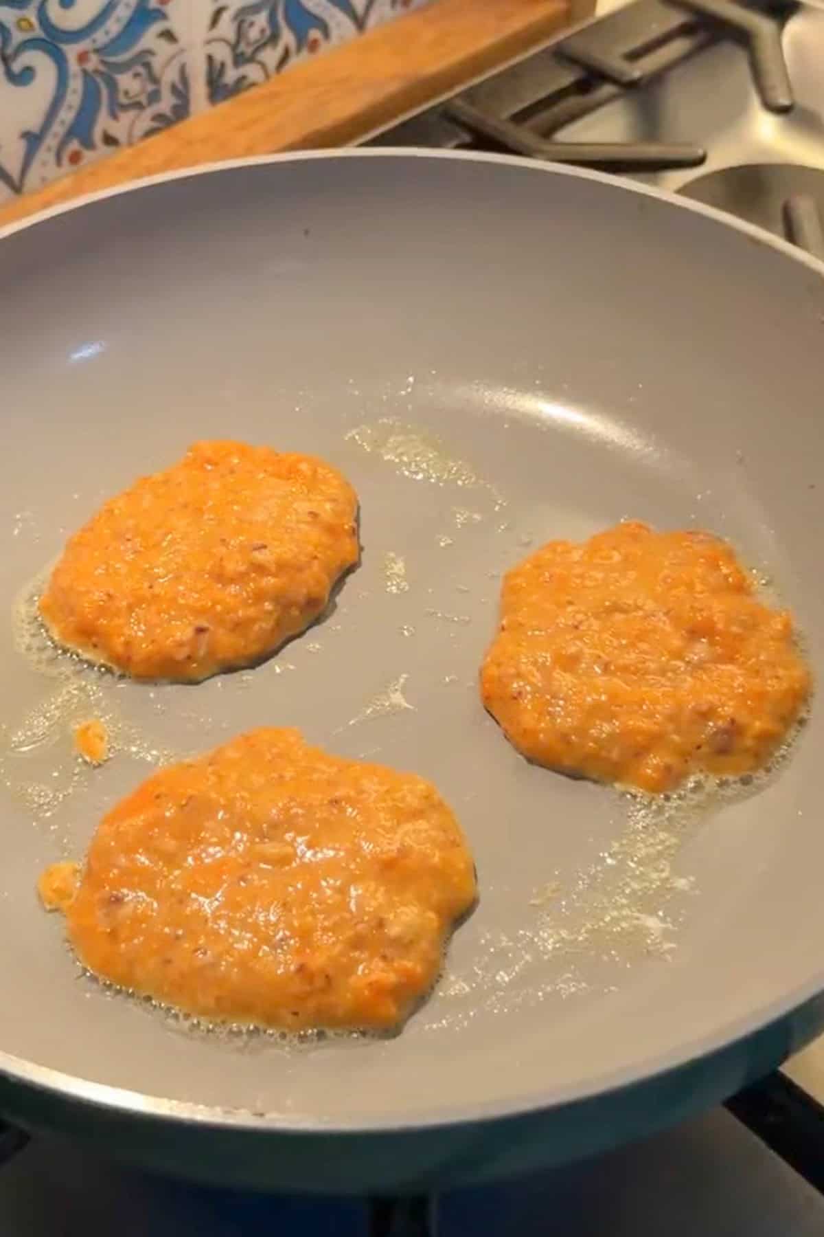 Three sardine pancakes cooking in a nonstick pan.